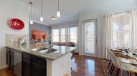This single-floor residence offers a cohesive and stylishly designed living environment with modern finishes and an open, functional layout. The kitchen is a standout feature, equipped with dark espresso cabinetry, granite countertops, stainless steel appliances, a tile backsplash, and a central island with a double sink — all set atop rich hardwood-style flooring that extends throughout the main living areas. Pendant lighting above the island adds a contemporary touch.

The open-concept design connects the kitchen directly to the living room, which is bathed in natural light from multiple large windows dressed with neutral drapes. The living area offers a welcoming atmosphere with ample space for seating and entertaining. Adjacent to the living room, a formal dining area features generous proportions, tall windows, and elegant draping, ideal for hosting gatherings.

The residence includes multiple bedrooms, each with hardwood-style or plush carpeted flooring, crown molding, natural light from windows with exterior views, and tasteful décor accents. The bathroom is finished with granite countertops, dark cabinetry matching the kitchen, tile-surround bathtub, and hardwood-style flooring. A entry hallway with closet storage completes the practical layout of this well-rounded home.