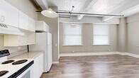 Located in the heart of downtown Fort Worth at 410 W 7th Street, this one-bedroom, one-bathroom unit offers a distinctive blend of industrial charm and functional living. The open-concept layout connects the kitchen and living area seamlessly, creating a bright and airy atmosphere enhanced by multiple windows that flood the space with natural light.

The kitchen is well-appointed with white cabinetry, ample counter space, a full-size range, refrigerator, and a dishwasher. Pendant lights hang from an exposed ceiling featuring whitewashed wood beams and industrial-style conduit, lending the space a loft-like character that sets it apart. Durable hardwood-style flooring runs throughout the main living areas, adding warmth and continuity.

The bedroom offers a comfortable and private retreat with carpeted flooring and an open upper overlook area accessed by a metal-railed staircase, adding vertical dimension to the unit. The bathroom includes a single-vanity with storage, tile flooring, a walk-in shower, and built-in shelving for added convenience.

Neutral, warm-toned walls throughout provide a versatile backdrop, while the architectural details — from the exposed beams to the industrial lighting track — give this downtown unit a uniquely characterful feel ideal for urban living.