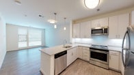 This single-floor residence showcases a thoughtfully designed open-concept layout that seamlessly connects the kitchen and living areas. The kitchen serves as a central highlight, featuring a large peninsula with granite countertops, an undermount sink, and pendant lighting overhead. White shaker-style cabinetry extends to the ceiling, offering generous storage, while stainless steel appliances—including a refrigerator, range, microwave, and dishwasher—provide a sleek, contemporary finish. Under-cabinet lighting and a clean tile backsplash add functional elegance to the space.

Wood-look plank flooring runs throughout the main living areas, contributing to a warm, cohesive aesthetic. The living room benefits from large windows fitted with blinds, allowing ample natural light to fill the space. Bedrooms are carpeted for comfort, with at least one featuring its own window with an exterior view.

The unit includes two bathrooms finished with neutral tile flooring, white vanities, and brushed nickel fixtures. Grab bars are incorporated into one bathroom, enhancing accessibility. A spacious walk-in closet with wire shelving and hanging rods provides practical storage. Overall, the space presents a clean, modern ambiance with a neutral color palette throughout.
