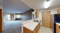 This single-floor unit offers a practical and comfortable layout with a seamless flow between its main living spaces. The kitchen is appointed with warm oak cabinetry, a tiled backsplash, stainless steel appliances including a refrigerator, range, and microwave, and a double-basin sink set into a peninsula with an extended breakfast bar. A pendant light fixture adds a refined touch above the counter. The kitchen opens directly to the living area, which features vaulted ceilings and soft carpeting, creating an airy and spacious feel. A large window brings in natural light and frames views of surrounding greenery. The unit includes multiple bedrooms, each finished with plush carpet, neutral-toned walls, and windows overlooking lush outdoor foliage. Two full bathrooms serve the unit, both featuring oak vanities with white countertops, tile flooring, and a tub-shower combination. The entry area is finished with durable tile flooring and provides convenient access to the kitchen. Throughout the unit, warm wood tones, neutral wall colors, and textured ceilings contribute to a cohesive and welcoming aesthetic, making this a well-appointed and functional living space.