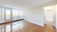 Located at 55 Brownlow Ave in Toronto's sought-after Davisville Village neighbourhood, Unit 1106 is a well-proportioned one-bedroom, one-bathroom residence spread across a single floor. The unit is defined throughout by warm, richly patterned parquet flooring that adds a timeless character to every room.

The living room is the heart of the unit, offering generous proportions and floor-to-ceiling vertical blinds that frame a sliding glass door opening onto a private balcony. From here, elevated treetop and open-sky views fill the space with natural light, creating a bright and airy atmosphere. Baseboard heating runs along the perimeter, ensuring comfortable warmth throughout the seasons.

The kitchen is tucked efficiently off the living area, featuring cabinetry with ample storage and a full-size refrigerator. A hallway connects the main living spaces to the bedroom and bathroom, providing a practical and well-organized layout.

The primary bedroom is a comfortable, quiet retreat with its own large window fitted with vertical blinds, offering continued green views and natural light. The bathroom is clean and classic in design, featuring a full soaker tub and shower combination with white subway tile surround and chrome fixtures. Overall, the unit offers a functional and inviting living environment in a prime Toronto location.