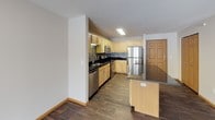 This single-floor, one-bedroom, one-bathroom unit is thoughtfully laid out to maximize comfort and functionality. The kitchen is a standout feature, showcasing light maple cabinetry, dark granite countertops, and a mosaic tile backsplash that adds visual texture. Stainless steel appliances — including a refrigerator, electric range, built-in microwave, and dishwasher — provide a modern, cohesive look. A peninsula with matching cabinetry and countertop offers additional prep space and serves as a natural divider between the kitchen and the rest of the living area. Wood-look flooring runs throughout the kitchen and entry areas, adding warmth and durability. The bedroom is a serene retreat, featuring plush carpeting, a ceiling fan with light fixture, and a large window that invites natural light and outdoor views. The full bathroom is clean and well-appointed, with a single-sink vanity with wood cabinetry, a tub-shower combination, and tile flooring. The overall layout, as seen in the dollhouse view, is open and efficient, with clear sightlines connecting the living, kitchen, and entry areas, making the space feel airy and easy to navigate.