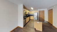 This single-floor, one-bedroom, one-bathroom unit is thoughtfully laid out to maximize comfort and functionality. The kitchen is a standout feature, showcasing light maple cabinetry, dark granite countertops, and a mosaic tile backsplash that adds visual texture. Stainless steel appliances — including a refrigerator, electric range, built-in microwave, and dishwasher — provide a modern, cohesive look. A peninsula with matching cabinetry and countertop offers additional prep space and serves as a natural divider between the kitchen and the rest of the living area. Wood-look flooring runs throughout the kitchen and entry areas, adding warmth and durability. The bedroom is a serene retreat, featuring plush carpeting, a ceiling fan with light fixture, and a large window that invites natural light and outdoor views. The full bathroom is clean and well-appointed, with a single-sink vanity with wood cabinetry, a tub-shower combination, and tile flooring. The overall layout, as seen in the dollhouse view, is open and efficient, with clear sightlines connecting the living, kitchen, and entry areas, making the space feel airy and easy to navigate.