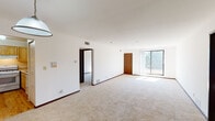 This single-floor unit offers a practical and comfortable layout designed to maximize usable living space. The open living and dining area is finished with plush wall-to-wall carpeting, crisp white walls, and dark wood trim accents that add warmth and definition throughout. A large sliding glass door floods the living area with natural light and provides direct access to an outdoor balcony or patio, while a pendant light fixture anchors the dining area.

The kitchen is equipped with light wood cabinetry offering ample storage, a gas range with overhead ventilation, a full-size refrigerator, and a stainless steel sink set into continuous countertops — all complemented by light hardwood flooring.

The unit includes two carpeted bedrooms, each with sliding-panel closets and generous windows that bring in natural light. One bedroom features convenient direct access to a full bathroom, which includes a tub/shower combination with warm-toned tile surround, a white vanity, and tile flooring. A second bathroom, finished in white with a lighted vanity mirror, provides added convenience for residents and guests.

Dark wood interior doors and consistent trim work carry a cohesive design language throughout the space, contributing to a clean and functional living environment.