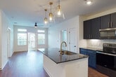 This thoughtfully designed single-floor residence showcases a contemporary aesthetic anchored by an open-concept layout connecting the kitchen and living areas. Rich hardwood-style flooring runs throughout the main living spaces, complementing the crisp white walls and creating a warm, inviting atmosphere.

The kitchen serves as the centerpiece of the space, featuring a large island with dark granite countertops and an undermount sink fitted with a brushed gold faucet. A trio of glass pendant lights with gold accents hang above the island, providing both task lighting and visual interest. Navy-blue shaker-style cabinetry with gold hardware extends to the ceiling, paired with a herringbone-pattern tile backsplash. Stainless steel appliances, including a refrigerator, range, and over-the-range microwave, complete the kitchen.

The living area extends toward glass doors that invite natural light and offer views of the surrounding exterior. Ceiling fans are present throughout for added comfort.

Bedrooms are carpeted and generously sized, with the primary suite featuring a walk-in closet and a private en-suite bathroom. The primary bath includes a double-sink vanity with granite countertops, gold faucets, a large mirror, and a separate glass-enclosed shower. A secondary bathroom features a soaking tub with tile surround and coordinating gold fixtures.