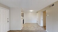 This single-floor residence offers a practical and thoughtfully arranged layout comprising one bedroom, two bathrooms, a living room, kitchen, and a dedicated closet. The living room is a generously sized, open area featuring neutral-toned carpet, a textured ceiling, and a large sliding glass door dressed with vertical blinds that invites natural light and provides outdoor views. The galley-style kitchen is efficiently designed with gray cabinetry, granite-patterned countertops, a tile backsplash, and black appliances including a range, microwave, and refrigerator, all set atop light wood-look flooring. The spacious primary bedroom features plush carpet, neutral walls, a window allowing natural light, and direct access to a sizable walk-in closet outfitted with multiple shelving units for ample storage. The bathroom includes a vanity with a granite-patterned countertop, a well-lit mirror, and a shower-tub combination. Throughout the unit, light wood-look flooring in main areas and soft carpet in living and sleeping spaces create a cohesive, comfortable aesthetic, complemented by textured ceilings and clean white trim.