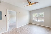 This single-floor residence in Saraland, Alabama offers a clean, modern aesthetic throughout its thoughtfully designed layout. The open living area is finished with light wood-style flooring and neutral gray walls, creating a bright and welcoming atmosphere. A ceiling fan with a built-in light fixture serves as a functional centerpiece overhead, while a large window with blinds allows natural light to fill the space with views of the surrounding greenery.

The living area flows seamlessly toward the kitchen, which is outfitted with white shaker-style cabinetry, white quartz countertops, and a full suite of stainless steel appliances including a refrigerator, electric range, over-the-range microwave, and dishwasher. A marble-style tile backsplash adds a refined touch, complementing the kitchen's crisp, contemporary design. A peninsula counter provides additional workspace and visual separation between the kitchen and living areas.

Adjacent to the kitchen, a generously sized closet with bi-fold doors offers ample storage. The bathroom is well-appointed with white cabinetry, a white quartz vanity top, a framed mirror, and a tiled shower-tub combination, all finished with light wood-style flooring that carries throughout the home. The overall design prioritizes clean lines, light tones, and practical functionality.