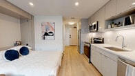Located at 4111 E Ninth Ave in Denver, Colorado, this single-floor studio unit offers a thoughtfully designed open-concept layout that maximizes functionality. Light hardwood flooring runs throughout the space, complementing the clean, modern aesthetic. A large floor-to-ceiling window along one wall floods the living and sleeping area with natural light while providing views of the surrounding neighborhood streetscape.

The kitchen is integrated seamlessly into the main living space and features glossy gray flat-front cabinetry extending to the ceiling for ample storage. Stainless steel appliances include a full-size electric range, over-the-range microwave, refrigerator, and dishwasher. White quartz countertops and a tile backsplash complete the polished look, with under-cabinet lighting adding functional illumination.

The sleeping area accommodates a full bed and benefits from a built-in storage wall with sliding panel doors, contributing to a clean, uncluttered environment. A dedicated bathroom off the main corridor includes a tub-shower combination, floating white vanity, and the same warm hardwood flooring found throughout. Recessed lighting and a neutral white-and-gray palette give the entire unit a bright, cohesive, and contemporary ambiance.