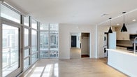 Located at 1810 State Street in San Diego, Unit #705 Plan A is a modern single-floor residence that showcases clean, contemporary design throughout. The open-plan living area is defined by expansive floor-to-ceiling windows framed in sleek gray aluminum, flooding the space with abundant natural light and offering views of the surrounding urban environment. Light-toned hardwood flooring runs throughout, complementing the crisp white walls and contributing to a bright, airy atmosphere.

A walk-in closet provides generous storage directly off the main living area, while a stacked washer and dryer unit housed behind louvered bifold doors offers convenient in-unit laundry. The layout flows efficiently, with a clear visual connection between the living space and adjacent rooms. HVAC is handled via a ceiling-mounted vent system, ensuring climate comfort year-round.

The overall ambiance is modern and minimalist, with an emphasis on natural light, open space, and functional design. The residence suits those seeking a contemporary urban lifestyle in a well-appointed San Diego location.