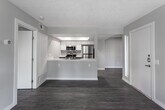 Located at 7600 Ambergate Pl in Riverside, California, this single-floor residence offers a thoughtfully updated interior with contemporary finishes throughout. Wood-look luxury vinyl flooring runs consistently through the living areas and bedrooms, contributing to a cohesive and modern aesthetic. The entry foyer welcomes you with a sidelight window beside the front door, allowing natural light to filter into the space.

The open-concept living area flows directly toward the kitchen, which is separated by a peninsula-style counter featuring a stainless steel undermount sink. The kitchen is equipped with stainless steel appliances, including a gas range, microwave, and refrigerator, complemented by white upper cabinetry and dark lower cabinets with sleek hardware. Recessed lighting within a tray ceiling highlights the kitchen workspace effectively.

The bedroom is a generously sized room with a ceiling fan, neutral gray walls, and access to both a walk-in closet with built-in shelving and a private bathroom. The bathroom features wood-look flooring, a modern vanity with a white countertop and dark cabinetry, a large mirror, and a full tub-shower combination with a curved curtain rod. Throughout the unit, soft neutral tones and clean lines create a calm and functional living environment.