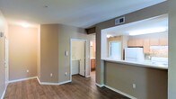 This single-story residence showcases an open, connected layout that promotes a comfortable flow between living spaces. The main living area features warm-toned walls paired with durable hardwood-style flooring, creating a cohesive and inviting ambiance throughout. Crisp white baseboards provide a clean contrast against the neutral palette.

The kitchen is positioned behind a pass-through counter with a breakfast bar, offering both functionality and an open connection to the main living space. Light wood cabinetry and white appliances, including a full-size refrigerator, contribute to a bright and practical cooking area illuminated by overhead lighting.

A dedicated in-unit laundry area is conveniently accessible directly from the main living space, housing a full-size washer and dryer — a practical feature that adds everyday convenience. Adjacent to the laundry area, a hallway leads to a bathroom finished with warm wood-toned cabinetry and a well-lit vanity mirror.

Ceiling vents are integrated throughout, ensuring efficient climate control. The overall design balances functionality with a clean, understated aesthetic, making the space feel well-organized and move-in ready.