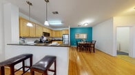 Located at 1920 Dunlap Crescent in Chester, Virginia, this single-floor residence offers a well-designed, open layout with consistent hardwood flooring throughout the main living areas. The kitchen serves as a central hub, featuring light maple cabinetry, dark granite countertops, stainless steel appliances, and a breakfast bar with pendant lighting overhead that comfortably seats multiple guests. The kitchen flows directly into a dedicated dining area, accented by a bold teal feature wall that adds a distinctive pop of color to the space.

Adjacent to the dining area, the living room is bright and inviting, benefiting from large windows that allow generous natural light to fill the room. A glass door opens to an outdoor balcony, further enhancing the sense of openness. A freestanding fireplace serves as a functional focal point within the living room.

The bedroom is carpeted for comfort, featuring windows on multiple walls that allow ample natural light. It connects to a spacious walk-in closet with built-in wire shelving and a full bathroom equipped with a single-sink vanity, light maple cabinetry, and tile flooring. The overall aesthetic is clean, neutral, and move-in ready.
