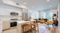 Located at 21010 Erwin St, this thoughtfully designed 2-bedroom, 2-bathroom unit offers a well-appointed single-level layout with modern finishes throughout. The open-concept kitchen and living area serves as the heart of the home, featuring a central island with seating, sleek light wood cabinetry, glossy upper cabinets, a white quartz countertop, and stainless steel appliances. Light hardwood flooring flows seamlessly through the entire unit, enhancing the bright, airy atmosphere created by recessed lighting and large windows. The living room benefits from elevated ceilings that add a sense of spaciousness, along with access to a private balcony overlooking a landscaped courtyard. The primary bedroom is a comfortable retreat with a dedicated closet and clean, neutral finishes. The second bedroom is similarly appointed. Both bathrooms are finished with white tile, including a full tub-shower combination in one, complemented by contemporary brushed metal fixtures and wood-toned flooring. A hallway connects the bedrooms and bathrooms, with two closets providing practical storage. The overall design is clean and contemporary, balancing functionality with a warm, inviting aesthetic suited for modern living.