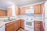 This two-story home in Madison, Wisconsin offers a well-designed layout across two floors. The main level features a combined kitchen and living room area, where rich hardwood-style flooring flows throughout. The kitchen is equipped with warm wood cabinetry, a breakfast bar, and white appliances, opening conveniently to the living area. The living room is generously sized, featuring plush carpeting and a sliding glass door that invites natural light and outdoor access. A staircase leads to the upper level, which is highlighted by a skylight that floods the landing with daylight and vaulted ceilings that add a sense of openness. The spacious primary bedroom features soaring vaulted ceilings, dual windows offering views of the surroundings, a ceiling fan, and soft carpeting. The second bedroom also features vaulted ceilings and ample space. Both bathrooms are well-appointed with warm wood vanities, white countertops, full tub-shower combos, and hardwood-style flooring. A dedicated closet provides additional storage. The home's neutral color palette, consistent trim work, and thoughtful use of natural light create a clean, welcoming ambiance throughout.