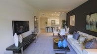 This single-floor residence offers a thoughtfully designed open-concept layout that seamlessly integrates the living, dining, and kitchen areas into one cohesive, flowing space. The living area features plush carpeting, a sleek media console, and a comfortable sofa accented with blue decorative vases on a dark wood coffee table, creating a stylish and inviting atmosphere. A bold dark feature wall adds depth and contrast to the otherwise bright, neutral color palette.

The dining area sits at the heart of the space, furnished with a white dining set that bridges the gap between the living room and the kitchen. The kitchen is well-appointed with white cabinetry, stainless steel appliances, pendant lighting, and a breakfast bar with bar stools, making it ideal for both casual dining and entertaining. Track lighting runs across the kitchen ceiling, providing focused illumination throughout the space.

Throughout the residence, recessed lighting and clean architectural lines contribute to a polished, modern aesthetic. The open floor plan maximizes the sense of space, allowing natural sightlines from the living area all the way to the kitchen. The overall ambiance is contemporary and welcoming, with a careful balance of light tones and bold accents that lend the space a refined, move-in-ready character.