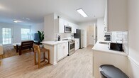 This single-floor residence offers a thoughtfully designed layout that balances comfort and functionality throughout its well-organized spaces. The open-concept living area features light wood-look flooring, a ceiling-mounted HVAC vent, and a glass-paneled exterior door that invites natural light into the room. The space comfortably accommodates a seating arrangement anchored by a woven area rug, with room for a media console and accent greenery.

The kitchen is finished with crisp white shaker-style cabinetry, subway tile backsplash, and a clean white countertop that extends into a breakfast bar with barstool seating—ideal for casual dining or conversation. Stainless steel appliances complement the bright, modern aesthetic.

The adjacent dining area features recessed lighting, chair-rail molding along the walls, and light wood flooring, creating an inviting space for seated meals. The bedroom is a serene retreat with a ceiling fan, natural light from a window with blinds, and a walk-in closet outfitted with wire shelving for organized storage.

The bathroom is cleanly finished with a white vanity, white countertop, wood-framed mirror, and wood-look tile flooring. A dedicated laundry room includes washer and dryer hookups, a dryer vent, and an overhead wire shelving system, rounding out this efficiently designed residence.