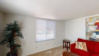 This single-floor unit is thoughtfully arranged to maximize functionality across its key living spaces. The living room serves as the heart of the home, featuring neutral-toned carpet, white walls, and a generously sized window fitted with horizontal blinds that allow natural light to filter in while maintaining privacy. A textured ceiling adds subtle character to the room, which comfortably accommodates a seating area alongside a small accent table.

The kitchen is efficiently designed with a galley-style layout, featuring light wood cabinetry, white laminate countertops, and a double-basin stainless steel sink. Wood-look flooring runs throughout this space, and a window above the counter brings in additional natural light. White appliances, including a refrigerator, dishwasher, and range, are seamlessly integrated into the cabinetry.

The bedroom is a calm, carpeted retreat equipped with a ceiling fan and light fixture, and a window dressed with sheer curtains that soften incoming light. The room offers ample space for standard bedroom furnishings.

The bathroom is straightforwardly appointed with a full tub-and-shower combination, a patterned curtain, a toilet, and a single vanity sink, completing this practical and livable unit.