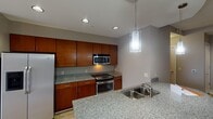 Located at 200 S Dawson St in the heart of Raleigh, NC, this single-floor unit offers a well-designed open-concept layout with contemporary finishes throughout. The kitchen is a standout feature, equipped with rich cherry wood cabinetry, granite countertops, and a full suite of stainless steel appliances including a refrigerator with ice maker, range, and built-in microwave. A curved peninsula with an undermount double sink and elegant pendant lighting serves as the centerpiece, seamlessly connecting the kitchen to the living area. The living space is bright and open, with hardwood-style flooring, a ceiling fan, and floor-to-ceiling sliding glass doors that lead to a balcony with urban views of the surrounding Raleigh cityscape. The bedroom offers plush carpeting, a tray ceiling with a ceiling fan, and a window that brings in natural light. The bathroom continues the granite aesthetic with a matching vanity, tile flooring, and a clean, functional layout. Neutral tones in warm gray throughout create a cohesive and modern ambiance, making this a well-appointed urban residence in one of Raleigh's vibrant downtown neighborhoods.