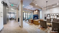 Located at 1001 W Main St in the heart of Durham, NC, this thoughtfully designed single-floor common area delivers an impressive blend of modern aesthetics and functional spaces. The entry foyer immediately sets the tone with floor-to-ceiling glass walls that flood the space with natural light and provide open views of the surrounding streetscape. A dramatic reception desk anchors the entrance, clad in a teal textured finish beneath a warm wood-slat ceiling and a distinctive cityscape wall art installation.

The main lounge area features herringbone-patterned hardwood flooring, elevated ceilings, and a full-height reclaimed wood fireplace surround that serves as a focal point for the comfortable seating arrangement of tufted sofas, leather armchairs, and sculptural accent tables. Artistic pendant chandeliers and track lighting add warmth and visual interest throughout.

A secondary lounge offers a more intimate gathering space with a large flat-screen television, curated artwork, and stylish furnishings. The dedicated conference room is outfitted with a solid wood boardroom table, ergonomic seating, a wall-mounted display, whiteboard, and a sculptural LED chandelier, with a glass partition wall providing both visibility and acoustic separation. The overall ambiance is polished yet inviting, combining urban sophistication with approachable comfort.