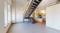 Located at 802 Olive St in downtown St. Louis, this two-bedroom, three-bathroom loft spans two floors of thoughtfully designed living space. The main level features large-format tile flooring, soaring ceilings, and an open-concept layout anchored by a dramatic open-tread steel and wood staircase with wire mesh railings. The kitchen is well-appointed with warm wood cabinetry, granite countertops, a tile backsplash, stainless steel appliances, a central island, and stylish pendant lighting. Exposed ductwork along the ceiling reinforces the space's industrial character. Ascending to the upper level, whitewashed exposed brick walls and painted structural beams create a striking loft aesthetic, while tall, multi-pane windows flood the space with natural light and frame panoramic views of the St. Louis skyline. The primary bedroom is generously proportioned, offering city views and tile flooring. The second bedroom features carpeting, exposed ceiling beams, and a built-in closet. Three well-appointed bathrooms include tub-shower combinations with clean white tile finishes. A stacked in-unit washer and dryer with adjacent shelving provides convenient laundry access. This urban loft masterfully blends industrial heritage with modern comfort.