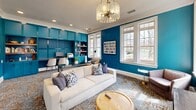 This 600 square foot resident lounge in Charlotte, NC, offers a striking blend of style and functionality. The space is dominated by bold teal walls, creating a vibrant and energetic atmosphere. Large windows allow ample natural light to flood the room, enhancing the airy feel and providing views of the surrounding area.

The lounge is thoughtfully divided into distinct areas for various activities. A comfortable seating area features a plush white sofa adorned with patterned pillows, perfect for relaxation. Adjacent to this is a sleek work area with built-in teal cabinetry and shelving, offering residents a stylish space for productivity.

The room's centerpiece is an elegant chandelier with cascading crystals, adding a touch of sophistication to the modern design. Recessed lighting throughout ensures even illumination. The flooring is a unique, textured carpet with a metallic sheen, adding depth and interest to the space.

Additional seating options include armchairs and stools, allowing for flexible use of the space. A large flat-screen TV mounted on the wall provides entertainment, while decorative elements like colorful artwork and plants add warmth and personality to the room.

This well-designed lounge seamlessly blends comfort, style, and practicality, creating an inviting communal space for residents to work, socialize, and unwind.