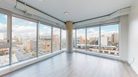 Located at 46 Flora St in Ottawa's vibrant Centretown neighbourhood, this contemporary 2-bedroom, 1-bathroom unit offers a bright and efficiently designed single-floor layout. The open-concept living, dining, and kitchen area is the centrepiece of the space, anchored by dramatic floor-to-ceiling windows wrapping two walls around a striking exposed concrete column. These expansive windows flood the area with natural light and frame impressive panoramic views of the Ottawa skyline and surrounding cityscape. Light-toned wood-style flooring runs throughout the unit, complementing the clean white walls and modern finishes that give the space a crisp, minimalist aesthetic. Both bedrooms are well-proportioned, each benefiting from large windows with city views and closet storage. The primary bedroom features a sliding door closet and access to an adjacent hallway leading to the full bathroom, which is finished with large-format tile flooring, a wall-mounted vanity with mirror, and clean contemporary fixtures. The unit also includes in-suite laundry and multiple additional closets for generous storage. The overall ambiance is sleek and modern, making it a practical and stylish urban residence in the heart of Ottawa.