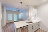 Located in Spring, TX, this thoughtfully designed one-bedroom, one-bathroom unit offers an efficient and modern living experience across a single floor. The open-concept kitchen and dining area serves as the heart of the space, featuring white shaker-style cabinetry with matte black hardware, a white quartz peninsula countertop with an undermount sink and black faucet, a subway tile backsplash, and a full suite of stainless steel appliances including a refrigerator, range, microwave, and dishwasher. Two sleek glass pendant lights hang above the peninsula, complementing the recessed ceiling lighting. Light wood-look flooring flows seamlessly throughout the unit, adding warmth and visual continuity. The living area benefits from abundant natural light through large windows dressed with horizontal blinds, and a ceiling fan overhead. The bedroom is a comfortable and well-proportioned retreat, also featuring a ceiling fan, a window for natural light, and direct access to the closet. The bathroom is finished with a white quartz vanity, white cabinetry with black hardware, a large mirror, and a tiled shower and tub combination. Stylish dark-toned double doors add a distinctive design accent. The overall aesthetic is clean, contemporary, and move-in ready.