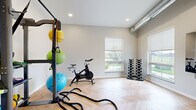 Located at 5532 38th St S in Fargo, North Dakota, this dedicated fitness and yoga studio is a well-appointed single-room space designed to support a comprehensive workout experience. The studio features striking herringbone-patterned hardwood flooring that lends a polished, modern aesthetic to the interior. Neutral gray walls and a clean white ceiling create a bright, focused environment conducive to both high-energy workouts and mindful practice.

Natural light flows in through multiple windows fitted with roller shades, offering views of the surrounding neighborhood while allowing for easy light control. An exposed industrial-style ductwork element along the ceiling adds a subtle modern-industrial character to the space.

The studio is equipped with a Smart functional training rack stocked with resistance bands, yoga mats, and stability balls in various sizes, alongside battle ropes for high-intensity training. A spin bike provides cardio options, while a set of tiered dumbbell racks offers a full range of free weights for strength training. A wall-mounted Reflect interactive mirror delivers on-demand guided workout programming directly within the space.

A glazed interior door with black framing provides access, and recessed lighting supplements natural light. This studio delivers a fully functional, thoughtfully designed fitness environment in a compact, efficient footprint.