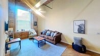 This 1210 square foot apartment in York, PA, offers a blend of industrial charm and modern comfort. The space boasts three bedrooms and three bathrooms, with the primary bedroom spanning a generous 260 square feet. The apartment's open-concept design seamlessly integrates the kitchen and living room, creating a spacious feel.

The kitchen features white cabinetry, a full-sized refrigerator, and essential appliances, complemented by a granite-topped island. The living area is adorned with a comfortable brown sofa and stylish decor, while large windows flood the space with natural light.

One of the bedrooms showcases exposed brick walls, adding character and texture to the space. High ceilings with exposed beams contribute to the loft-like atmosphere. The bathrooms are modern and well-appointed, with one featuring a shower-tub combination.

Throughout the apartment, you'll find a mix of carpeted and hardwood flooring. The decor is contemporary, with touches of nature-inspired art and furnishings. A dedicated workspace with a desk and chair is also available, perfect for those working from home.

This apartment combines the convenience of modern living with the charm of historic architecture, offering a unique and comfortable living experience in the heart of York.