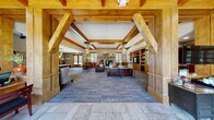 Located at 985 N Maple Grove in Boise, Idaho, this single-story clubhouse facility showcases a distinctive rustic-lodge aesthetic defined by prominent exposed timber beams, warm wood millwork, and stone accents throughout. The grand main entrance frames the expansive common lounge through a striking timber portal, where soaring beamed ceilings and pendant cluster lighting create an inviting, lodge-inspired atmosphere. The centerpiece of the lounge is a floor-to-ceiling stacked-stone fireplace with a substantial wood mantel, flanked by large windows that draw in natural light and views of surrounding greenery. Built-in wood shelving with an integrated television provides a functional and stylish focal point on the opposite wall, while generous seating arrangements encourage gathering and relaxation.

Adjacent to the main lounge, a well-appointed reception area features warm wood paneling, leather sofas, and additional seating nooks. A fully equipped kitchen includes a large granite-topped island with bar seating, stainless steel appliances, warm wood cabinetry, and contemporary pendant lighting. Dedicated workspace alcoves offer natural light and wood-trimmed window seating. The facility also includes a well-equipped fitness center with multiple cardio and strength-training machines, illuminated by large windows. The overall ambiance is warm, functional, and cohesive throughout.