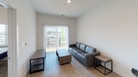 This single-floor unit offers a clean, contemporary design throughout, with light hardwood-style flooring and crisp white walls creating a bright and cohesive aesthetic. The kitchen is a functional centerpiece, featuring dark espresso cabinetry, granite countertops, a stainless steel sink, and a full suite of stainless steel appliances including a range, microwave, and refrigerator. Recessed lighting and ample upper cabinet storage complete the space. The living area is welcoming and airy, benefiting from natural light that pours in through a sliding glass door that opens to a private balcony, offering views of the surrounding area. The bathroom maintains the same refined finishes found throughout, with a granite-topped dark wood vanity, wood-look flooring, and clean neutral walls. A dedicated laundry area houses a stacked Whirlpool washer and dryer unit alongside built-in shelving, adding practical convenience. The overall layout is efficient and thoughtfully designed, with a neutral palette and consistent use of quality materials that give the space a polished, modern character.