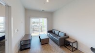 This single-floor unit offers a clean, contemporary design throughout, with light hardwood-style flooring and crisp white walls creating a bright and cohesive aesthetic. The kitchen is a functional centerpiece, featuring dark espresso cabinetry, granite countertops, a stainless steel sink, and a full suite of stainless steel appliances including a range, microwave, and refrigerator. Recessed lighting and ample upper cabinet storage complete the space. The living area is welcoming and airy, benefiting from natural light that pours in through a sliding glass door that opens to a private balcony, offering views of the surrounding area. The bathroom maintains the same refined finishes found throughout, with a granite-topped dark wood vanity, wood-look flooring, and clean neutral walls. A dedicated laundry area houses a stacked Whirlpool washer and dryer unit alongside built-in shelving, adding practical convenience. The overall layout is efficient and thoughtfully designed, with a neutral palette and consistent use of quality materials that give the space a polished, modern character.