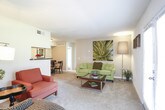 This single-floor residence offers a thoughtfully designed layout with clearly defined living spaces that flow naturally from one area to the next. The living room serves as the heart of the home, featuring plush carpeting, a set of French doors that invite natural light and provide outdoor access, and ample room for comfortable seating arrangements. A half-wall partition subtly separates the living area from the dining space, where a rounded table and seating set are positioned beneath flush-mount lighting, creating an intimate setting for meals.

The galley-style kitchen is efficiently organized with light wood cabinetry lining both sides, dark granite-style countertops, tile flooring, and black appliances including a refrigerator, range, microwave, and dishwasher. Track lighting illuminates the workspace throughout.

Two well-proportioned bedrooms each feature soft carpeting, ceiling fans with light fixtures, and natural light from windows dressed with sheer curtains and blinds. One bedroom includes a walk-in closet with built-in shelving. Both bathrooms are finished with tile flooring, light wood vanities, dark countertops, and shower-tub combinations.