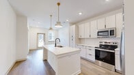 Located at 20 Graf Dairy Dr in Mobile, AL, this thoughtfully designed single-story residence offers a clean, contemporary aesthetic throughout. The open-concept kitchen and living area serves as the heart of the home, highlighted by a large center island with a white quartz countertop, an undermount sink with a matte black faucet, and elegant gold-accented pendant lights overhead. Crisp white cabinetry with black hardware lines the kitchen walls, complemented by a herringbone tile backsplash and a full suite of stainless steel appliances, including a refrigerator, range, and microwave. Light wood-tone flooring flows through the main living and kitchen areas, while recessed lighting keeps the space bright and airy. A private entry door with a window allows additional natural light into the open living zone. The bedroom offers plush carpeting, large windows with exterior views, and a ceiling fan, creating a comfortable and sunlit retreat. Three closets provide generous storage throughout the unit. The bathroom features warm wood-toned cabinetry, a white vanity countertop, a framed mirror, matte black fixtures, and light wood-look flooring, delivering a polished and cohesive finish.