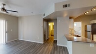 This single-floor residence offers a thoughtfully designed open-concept layout that seamlessly connects the living area and kitchen. The living space is generously proportioned, featuring durable wood-look flooring in a warm neutral tone, crisp white baseboards, and a ceiling fan. A sliding glass door with vertical blinds fills the room with natural light and provides outdoor access. The galley-style kitchen is well-equipped with stainless steel appliances — including a refrigerator, electric range, and built-in microwave — complemented by white shaker cabinetry, a classic subway tile backsplash, dark countertops, and a stainless steel sink. A peninsula with counter seating bridges the kitchen to the living area, enhancing the open flow. The bedrooms continue the wood-look flooring and feature ceiling fans, natural light from window blinds, and access to walk-in closet space. The bathroom is finished with a white vanity, dark countertop, and a full tub-shower combination with a rainfall showerhead. A dedicated laundry area accommodates a full-size, side-by-side washer and dryer with built-in overhead shelving. Throughout, the neutral color palette and modern finishes create a clean, cohesive, and functional living environment.