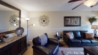 This single-floor residence offers a thoughtfully arranged layout that balances comfort and functionality across its key living areas. The living room serves as the heart of the home, featuring plush carpeted flooring, a textured ceiling, a ceiling fan, and a chair rail that runs along the walls, lending a refined architectural touch. Large vertical blinds frame a sliding door, allowing natural light to filter into the space. Adjacent to the living room, the dining area continues the warm aesthetic with rich hardwood-style flooring, a classic wooden dining table, and wall art that adds character to the space. A beam detail at the ceiling transition subtly defines the two areas. The galley-style kitchen is efficiently designed with white cabinetry, dark granite-look countertops, a double sink, white appliances including a stovetop range and refrigerator, and hardwood-style flooring, with a louvered pantry door providing additional storage. The bedroom is a serene retreat, complete with soft carpeting, a ceiling fan with light fixture, a window with decorative curtains, and ample space for dark wood furniture. The full bathroom features a tub-shower combination with tile surround, dark countertop vanity, and hardwood-style flooring, completing this cohesive and welcoming home.