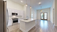 Located at 2001 Commerce St in the heart of Alpharetta, GA, this well-appointed 2-bedroom, 2-bathroom residence offers a thoughtfully designed single-level floor plan with a bright, modern aesthetic throughout. The open-concept living and kitchen area serves as the centerpiece of the home, featuring soaring ceilings, recessed lighting, and wood-look flooring that flows seamlessly throughout the main living spaces. The kitchen is outfitted with crisp white shaker cabinetry reaching to the ceiling, light quartz countertops, a classic subway tile backsplash, stainless steel appliances, and a center island with an undermount sink illuminated by elegant pendant lighting. The living room is anchored by French doors that flood the space with natural light and provide outdoor access, complemented by a ceiling fan and generous vertical wall space. Both bedrooms are carpeted and well-lit with natural light, while the primary bedroom connects to a spacious en-suite bathroom featuring a dual vanity, large-format tile flooring, and a glass-enclosed shower. Three closets — including a generously sized walk-in with wire shelving — provide ample storage. The building features a beautifully landscaped courtyard with lush greenery and comfortable seating, creating an inviting outdoor retreat.