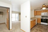 This single-floor residence offers a practical and well-organized layout that maximizes everyday comfort. The open-concept design connects the kitchen and living area seamlessly, creating a cohesive and functional living space. The kitchen is equipped with warm honey-toned wood cabinetry, ample counter space, a coil-top electric range, a built-in microwave, and a full-size refrigerator. The flooring throughout the kitchen features earth-toned stone-look tile, adding a grounded, neutral aesthetic. A breakfast bar separates the kitchen from the living area, which is finished with plush beige carpeting and a textured ceiling. A ceiling fan overhead provides additional air circulation, while a large sliding glass door opens to a private balcony with decorative wrought iron railing, bringing in natural light and scenic outdoor views of surrounding trees. The bedroom continues the carpeted flooring and is fitted with its own ceiling fan, a baseboard heater, and a window that frames views of the natural surroundings. The full bathroom features the same stone-look tile as the kitchen, a standard toilet, a vanity with wood cabinetry, and a full-size tub and shower combination enclosed by a clean white surround. Throughout the unit, neutral tones and consistent finishes create a cohesive, move-in-ready environment.