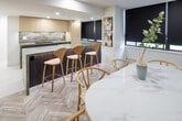 Located at 2 Edith Dr in Toronto's desirable Midtown neighbourhood, this thoughtfully designed single-floor space showcases a refined, contemporary aesthetic throughout. The open-concept layout seamlessly connects the kitchen, dining, and living areas, creating a cohesive and functional environment.

The kitchen is outfitted with light wood cabinetry, stone countertops featuring a textured finish, a matte black undermount sink paired with a brushed gold faucet, and under-cabinet LED lighting that adds a warm, ambient glow. A central island with a contrasting dark stone finish and bar seating provides additional workspace and casual dining.

The dining area is anchored by a white oval table surrounded by natural wood wishbone-style chairs, all set atop a distinctive light herringbone-patterned floor. A row of large windows fitted with sleek dark roller blinds lines the perimeter, allowing for controlled natural light.

The living area features a bold, dark accent wall with a wall-mounted television and open shelving, creating a striking focal point. A curved charcoal bouclé sofa, marble coffee table, and vibrant yellow accent seating add personality and depth. Slatted wood paneling provides elegant textural contrast. Recessed lighting throughout ensures a clean, polished ceiling line across the entire space.