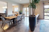 Located at 402 Highway 23 NW in Suwanee, Georgia, this single-floor community clubhouse offers a well-appointed and versatile gathering space designed with a contemporary aesthetic. Polished concrete floors run throughout, providing a sleek, cohesive foundation that complements the modern interior design.

The open-plan layout encompasses several distinct functional zones. A spacious lounge and seating area provides comfortable furnishings ideal for relaxed socializing, while a dedicated game room features a full-length shuffleboard table and wall-mounted television, perfect for recreational gatherings. A cozy booth-style nook with pendant lighting offers an intimate setting for smaller groups.

The catering-style kitchen is a standout feature, with rich butcher block countertops lining both sides of a galley-style corridor, paired with crisp cabinetry, a utility sink, and multiple under-counter beverage refrigerators. An elegant chandelier adds a refined touch overhead.

The dining area is anchored by a solid wood communal table surrounded by striped upholstered chairs, set against a textured mosaic tile accent wall. French doors flood the space with natural light and open directly to an outdoor pool and patio area, seamlessly connecting indoor and outdoor entertaining. Tall decorative planters with live indoor trees add a vibrant, organic element throughout the space.