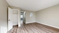 Located at 1911 S Haster St in Anaheim, California, this two-story home offers five bedrooms and two bathrooms across two evenly distributed floors connected by a staircase. The interior features a consistent, clean aesthetic with warm neutral tones and white trim throughout.

The main floor includes a galley-style kitchen outfitted with white cabinetry, granite-look countertops, a double basin sink, and wood-look flooring — providing a functional and bright cooking space. Bedrooms on this level are generously sized, featuring the same wood-look flooring, soft beige walls, and built-in closets, with small interior pass-through windows adding a unique architectural detail.

Upstairs, the bedrooms transition to plush carpeting in a neutral tone, offering a comfortable and quieter retreat. The spacious primary bedroom includes a walk-in closet and wall sconce lighting. Both bathrooms are well-appointed; one features a full soaking tub with a marble-style tile surround, a white vanity with under-cabinet storage, and a large mirror, while the second bathroom is clean and compact with matching finishes.

Wood-look flooring runs throughout the main living areas and bathrooms, tying the space together cohesively. The home's layout is practical and efficient, with hallways connecting all rooms across both levels.