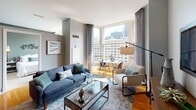 Located at 343 S Dearborn Street in Chicago's vibrant Loop neighborhood, this well-appointed single-floor residence combines modern urban design with comfortable living. The open-concept kitchen is outfitted with rich cherry wood cabinetry, granite countertops, a mosaic tile backsplash, black appliances, and a peninsula island with bar seating — ideal for casual dining and entertaining. Warm hardwood flooring flows throughout the main living areas, anchoring the space with a cohesive, inviting feel. The living room is bathed in natural light through large windows that frame striking views of Chicago's iconic downtown skyline, with floor-to-ceiling drapes adding an elegant touch. Two well-sized bedrooms offer distinct personalities: one features light blue walls, a built-in niche with track lighting, and plush carpeting, while the second showcases deep olive-green walls with contemporary wall art and a spacious closet. The bathroom is finished with tile flooring, a full tub and shower combination, a clean white vanity, and deep teal walls that lend a bold, spa-like atmosphere. Track lighting and thoughtful design details throughout reflect a cohesive modern aesthetic befitting this prime Chicago address.