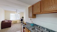 This single-floor unit at 341 presents a functional and well-organized layout across its living spaces. The open-concept design connects the kitchen directly to the living area, creating a seamless flow throughout the main space. The kitchen is equipped with warm oak cabinetry, a double-basin stainless steel sink, dark granite-style laminate countertops, and a white range, providing ample storage and prep space. A breakfast bar with seating adds a casual dining option. The living area features neutral carpet, cream-toned walls, and a ceiling fan with light fixture, contributing to a bright and airy atmosphere. A window at the far end of the living space invites natural light and offers views of surrounding trees. The bedroom is generously proportioned with plush carpet, a ceiling fan, and dual windows that frame outdoor scenery, enhancing the sense of openness. The bathroom includes a tiled walk-in shower and toilet, with ventilation overhead. Durable wood-look flooring runs through the kitchen and entry areas, while carpet adds comfort to the living and sleeping spaces. The unit's straightforward, single-level design makes it an accessible and easy-to-navigate living space.