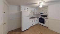 This single-floor unit offers a practical and straightforward layout across two bedrooms and one full bathroom. The floor plan reveals a well-organized arrangement of rooms, with clearly defined living, sleeping, and kitchen areas connected by a central hallway.

The kitchen is equipped with white cabinetry featuring black hardware, a full-size refrigerator, an electric range with an over-the-range microwave, and a double-basin sink. Countertops provide ample prep space, and tile flooring adds durability to the area.

Both bedrooms are carpeted and fitted with ceiling fans. The primary bedroom connects to an adjacent room and benefits from multiple windows that bring in natural light and outdoor views. The second bedroom is similarly carpeted with neutral walls, offering a clean and versatile space. Baseboard heating is present in at least one bedroom.

The bathroom features full white tile walls surrounding a tub-shower combination, a pedestal-style vanity with chrome fixtures, and a mirrored medicine cabinet with built-in shelving.

The living area is carpeted, features a textured ceiling, a ceiling fan with light, and a front entry door, providing a welcoming and functional common space throughout the unit.