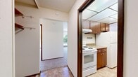 This ground-floor unit in Burien, WA offers a practical and well-organized single-level layout encompassing one bedroom, one bathroom, a living room, kitchen, closet, and two hallways. The interior features a textured ceiling throughout and plush carpet flooring in the living and sleeping areas, while the kitchen and bathroom utilize tile flooring for durability.

The kitchen is efficiently designed in a galley style, featuring warm brown cabinetry, a neutral countertop with an integrated sink, a white electric range, and a full-size refrigerator. A panel ceiling light provides bright, even illumination. The kitchen connects through a hallway to the dedicated closet, enhancing storage accessibility.

The living room is a bright, open space benefiting from abundant natural light through a large sliding glass door that opens to a private outdoor patio area bordered by mature greenery and a fenced perimeter. A baseboard heating system runs along the exterior wall, ensuring warmth year-round.

The bedroom features carpet flooring, a baseboard heater, and a generously sized window with views of the surrounding landscaping, filling the room with natural light. The bathroom includes a wide vanity countertop, an undermount sink, a large wall mirror, and a tub/shower combination with tile surround.