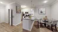 This single-floor residence offers a thoughtfully designed layout that balances comfort and functionality throughout. The open-concept living, dining, and kitchen area serves as the heart of the home, featuring wood-look flooring, crown molding, and a large sliding glass door that fills the living room with natural light. The kitchen is equipped with stainless steel appliances including a gas range, over-the-range microwave, and refrigerator, complemented by white shaker-style cabinetry, gray quartz countertops, and a peninsula with pendant lighting that provides additional prep and dining space. The adjacent dining area accommodates a full dining set with ease. The primary bedroom is generously sized, featuring a ceiling fan, warm-toned hardwood-style flooring, and direct access to a spacious walk-in closet outfitted with multi-tier wire shelving. The primary bathroom includes a white vanity, gray countertop, large framed mirror, and a tub-shower combination. The second bedroom is comfortable and well-lit, with its own nearby full bathroom that mirrors the clean, modern finishes found throughout the home. A dedicated laundry area houses a full-sized side-by-side washer and dryer. Neutral gray walls and consistent flooring unify the space with a cohesive, contemporary aesthetic.