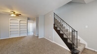 Located at 1000 S Woodlawn Blvd in Wichita, Kansas, this residential property offers a thoughtfully designed layout spread across multiple levels. The main living area welcomes visitors through a bold black front door, opening into a spacious, carpet-floored room bathed in natural light from a front-facing window. A striking staircase with dark wood steps and ornamental wrought-iron balusters serves as a focal point, while a built-in arched shelving unit adds both character and functional storage to the living space.

The kitchen is well-appointed with dark espresso cabinetry, light stone-look countertops, black appliances including a range and dishwasher, and light wood-look flooring. A sliding glass door leads directly to an outdoor patio area, filling the kitchen with natural light.

The bedrooms are generously sized, each featuring plush carpeting, ceiling fans, and large windows with vertical blinds that allow for ample natural light and outdoor views. Sliding closet doors provide convenient storage in the primary bedroom.

The lower level offers additional flexible living space, distinguished by wood-look plank flooring, textured walls, and a small window that brings in natural light, making it well-suited for a recreation room or home office.