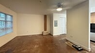Located at 1700 East Marshall Street in Richmond, Virginia, Unit 114 is a compact yet efficiently laid out space that blends industrial character with functional design. The main living area features polished concrete floors that lend an urban, loft-like aesthetic, complemented by crisp white walls and clean white baseboards. A wooden structural column adds a raw, architectural accent to the open floor plan. A ceiling fan provides overhead lighting and airflow, while a louvered closet door conceals an electrical panel. Natural light filters in through a window fitted with horizontal blinds, offering views of the surrounding neighborhood. A striking staircase with wooden treads and a sleek metal railing with vertical balusters connects the main level to an upper loft area. The upper level showcases a standout exposed wood-beam ceiling with dark crossbeams, adding warmth and texture to the space. This level includes plush carpeting, generous closet storage with wire shelving on both sides, a full bathroom with tile flooring, and a dedicated laundry area with a stacked washer and dryer unit. The combination of concrete and carpet flooring, exposed beams, and metal railings gives this unit a distinctive industrial-chic character well-suited to its Richmond location.