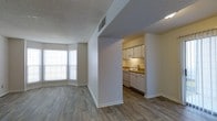 This single-story unit offers a practical and comfortable layout designed for everyday living. The living area is bright and open, benefiting from a large multi-pane window that allows generous natural light to fill the space. Wood-style hard-surface flooring runs throughout, adding warmth and visual continuity across the main living areas.

The kitchen is positioned adjacent to the living space, partially enclosed by a structural dividing wall that defines the two areas while maintaining a connected feel. It features white cabinetry, under-cabinet lighting, a countertop workspace with warm-toned laminate surfaces, and white appliances including a range and dishwasher. The layout is efficient, making the most of the available space.

A textured popcorn ceiling and neutral wall tones throughout contribute to a clean, understated aesthetic. HVAC ventilation is integrated into the ceiling for year-round climate control. The unit includes two bedrooms and one and a half bathrooms, offering functional accommodations suitable for a variety of living arrangements. White baseboards provide a crisp finish against the neutral flooring and walls.