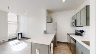 Located at 1216 N Superior St in Spokane, WA, this one-bedroom, one-bathroom unit offers a well-designed layout that makes efficient use of its cozy footprint. The open-concept kitchen is a standout feature, outfitted with sage-green cabinetry, stainless steel appliances including a range, microwave, and refrigerator, white quartz countertops, and a peninsula that doubles as a casual dining or workspace area. Light wood-look flooring runs throughout, complementing the crisp white walls and grey accent baseboards and doors that give the unit a clean, contemporary aesthetic. The living area is bathed in natural light, courtesy of large arched-top windows that frame views of the surrounding neighborhood and allow sunlight to pour across the floors. The bedroom is a comfortable, well-proportioned space with the same large windows and baseboard heating. The bathroom features a full tub-shower combo with large-format white subway tile, offering a clean and timeless look. A hallway and dedicated closet provide practical storage. Recessed lighting and modern hardware throughout round out the thoughtful design of this efficiently laid-out Spokane residence.